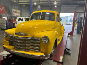 yellow classic Chevy on the lifts in the bay